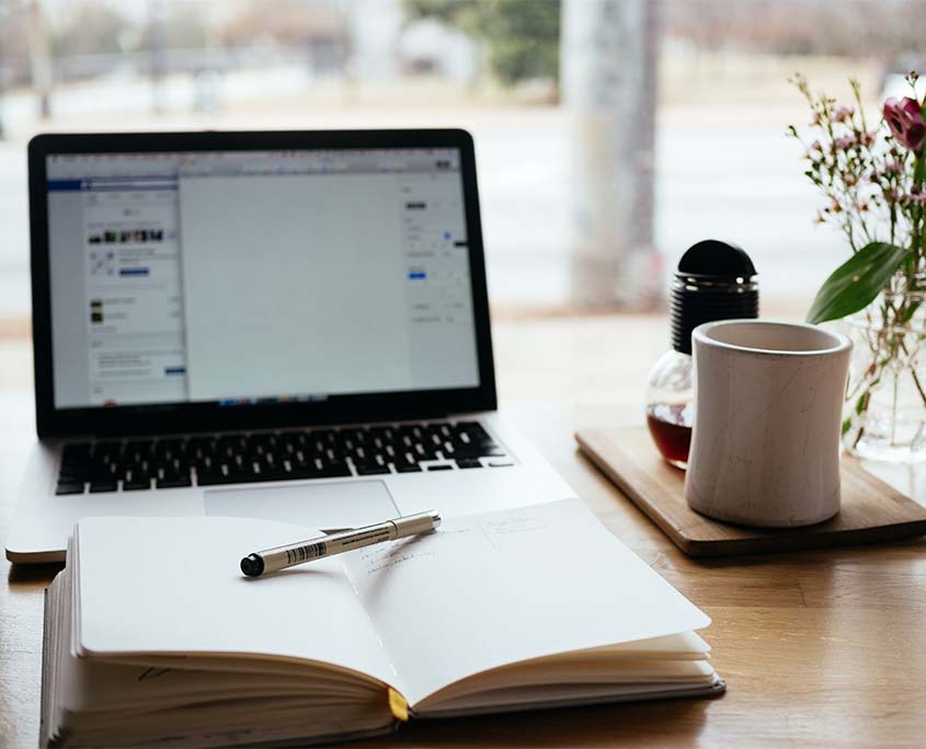 A photo of a pen on a notebook infront of a laptop.