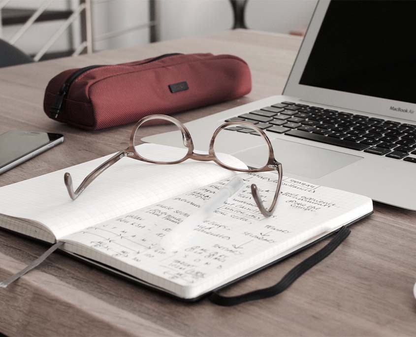 Photo of an eyeglass on a notebook near a laptop.