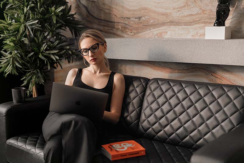 A photo of a woman using a laptop on her couch.